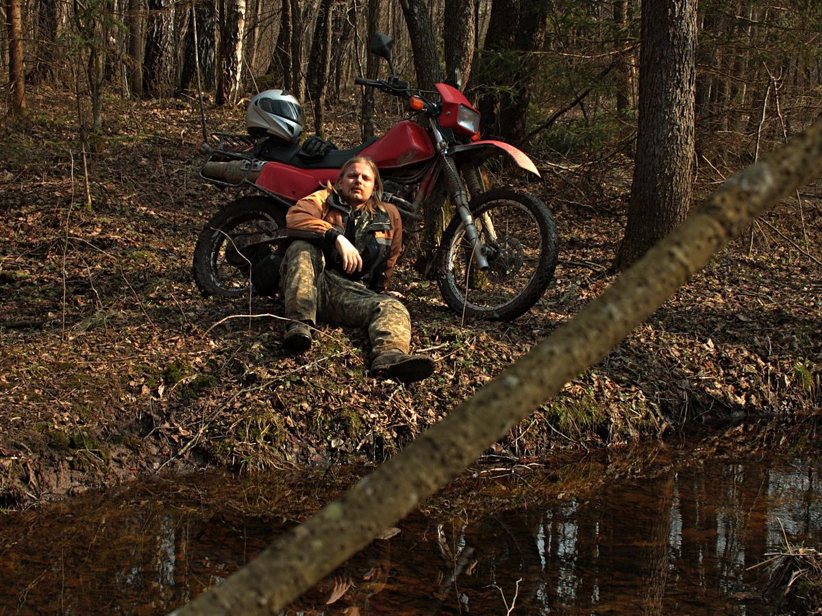 Мотоцикл и водитель возле ручья в лесу